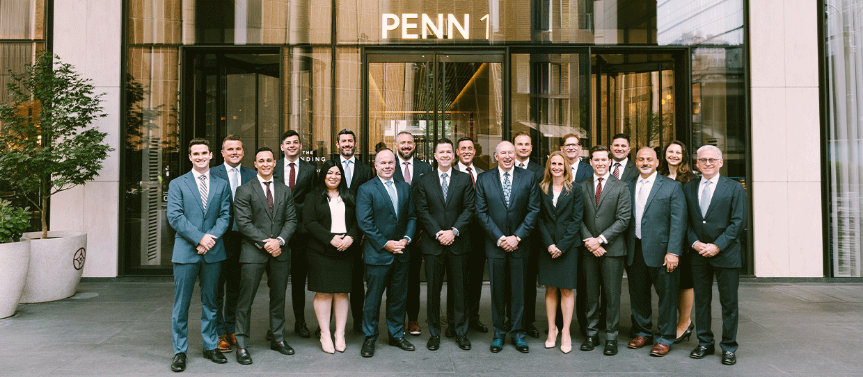 Group of injury attorneys posing for a photo outside a modern office building with 'PENN 1' above the entrance.